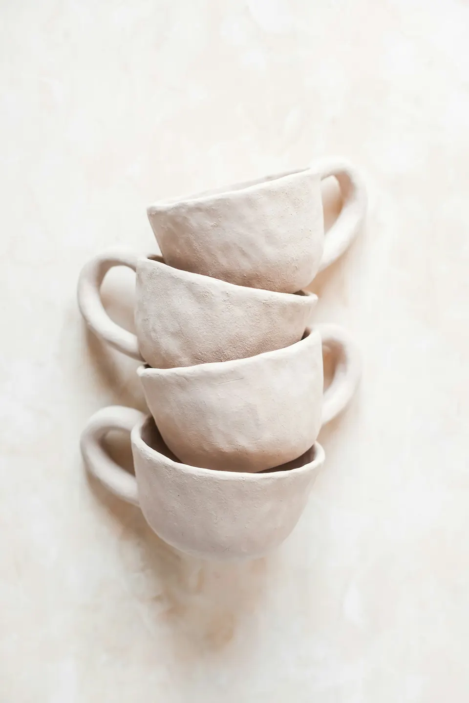 Four handmade cups stacked on a linen background