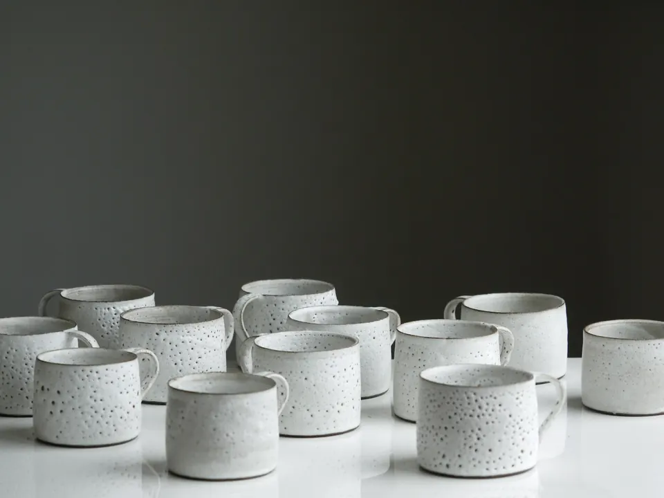 Rows of white speckled mugs on a dark background