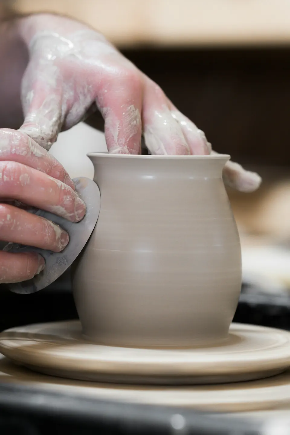 Hands shaping a pot on the wheel