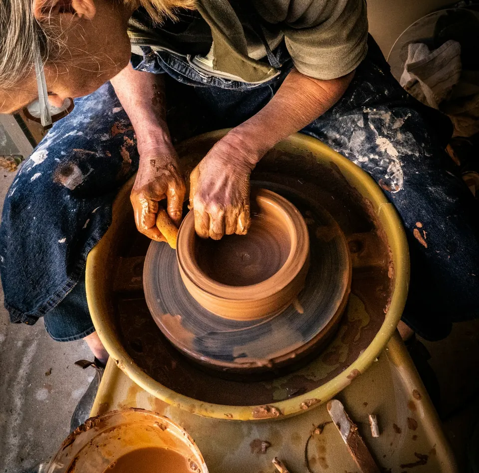A potter shaping a clay pot on a wheel, seen from above